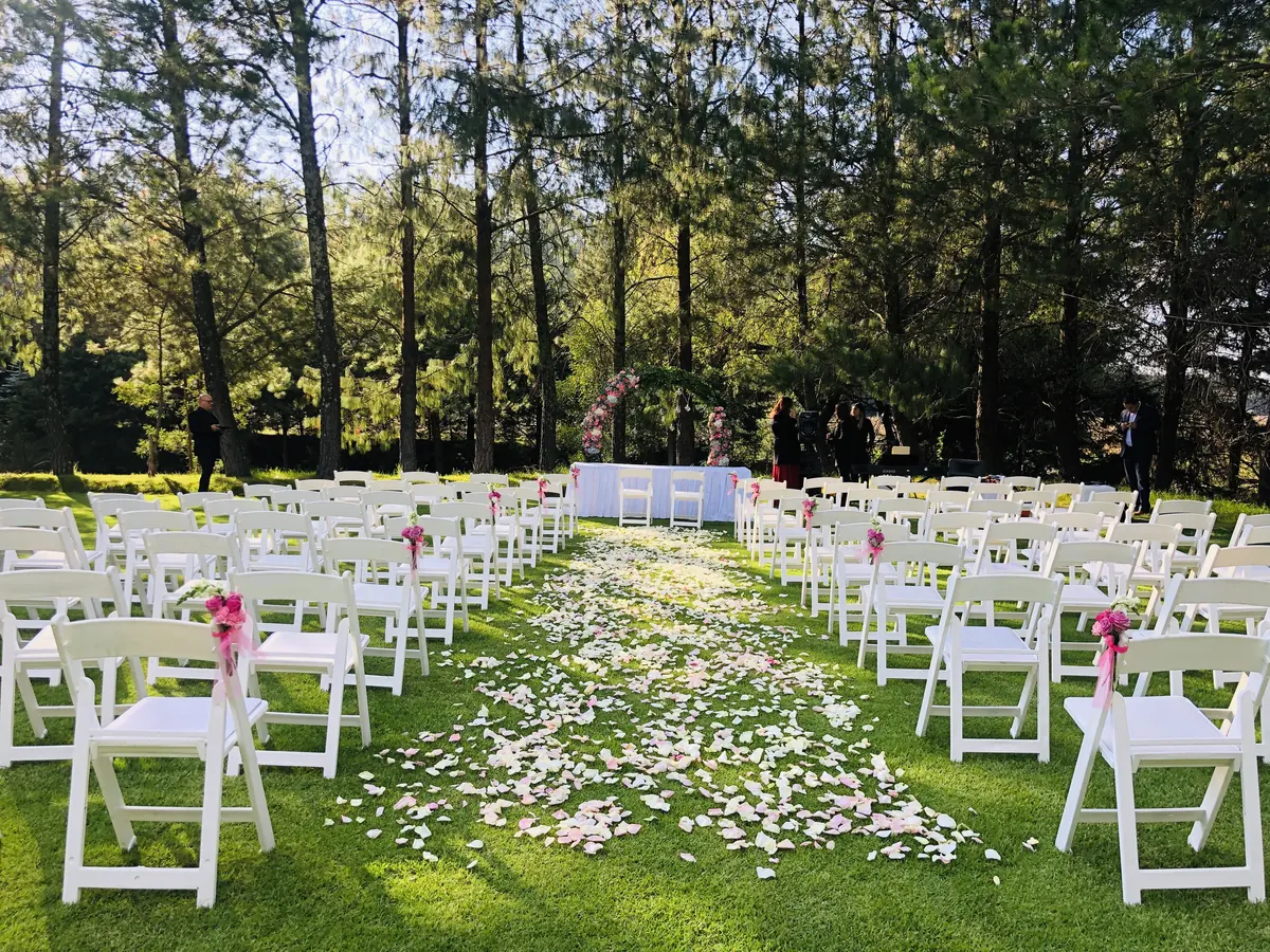 Ceremonia en jardín con sillas blancas y pasillo de pétalos