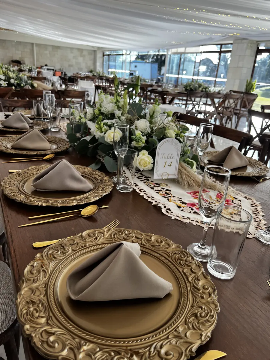 Plato base dorado labrado con servilleta y arreglo de flores blancas